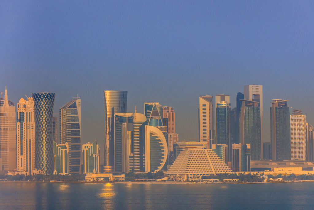 Skyline van Doha, Qatar, bij zonsopgang met moderne wolkenkrabbers en reflecties in het water.