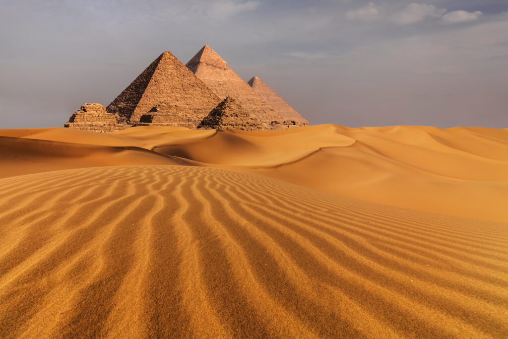 Zicht op de iconische piramides van Gizeh in Egypte, omgeven door uitgestrekte woestijnduinen bij zonsondergang.