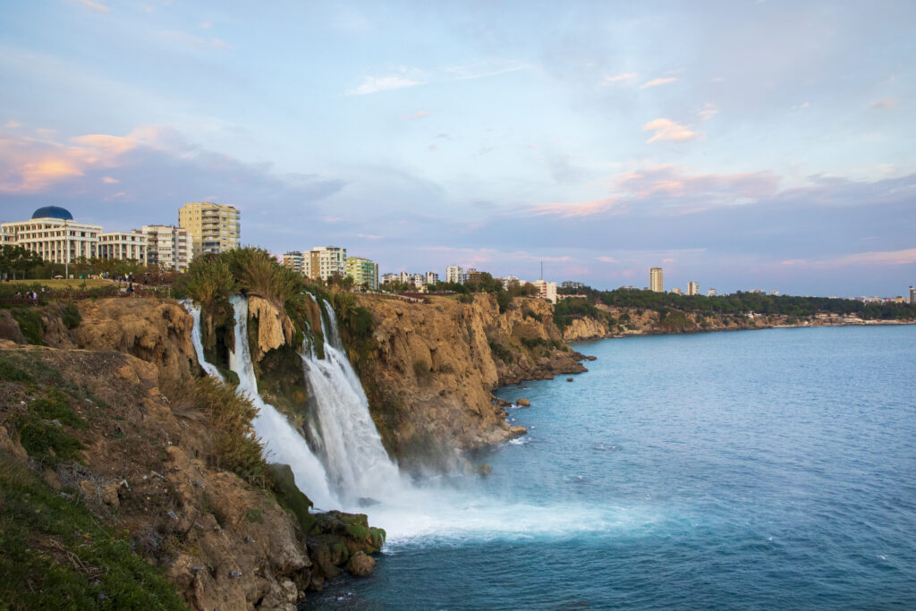 Uitzicht op de Düden-watervallen in Antalya, Turkije, met een prachtige kustlijn en moderne gebouwen op de achtergrond.